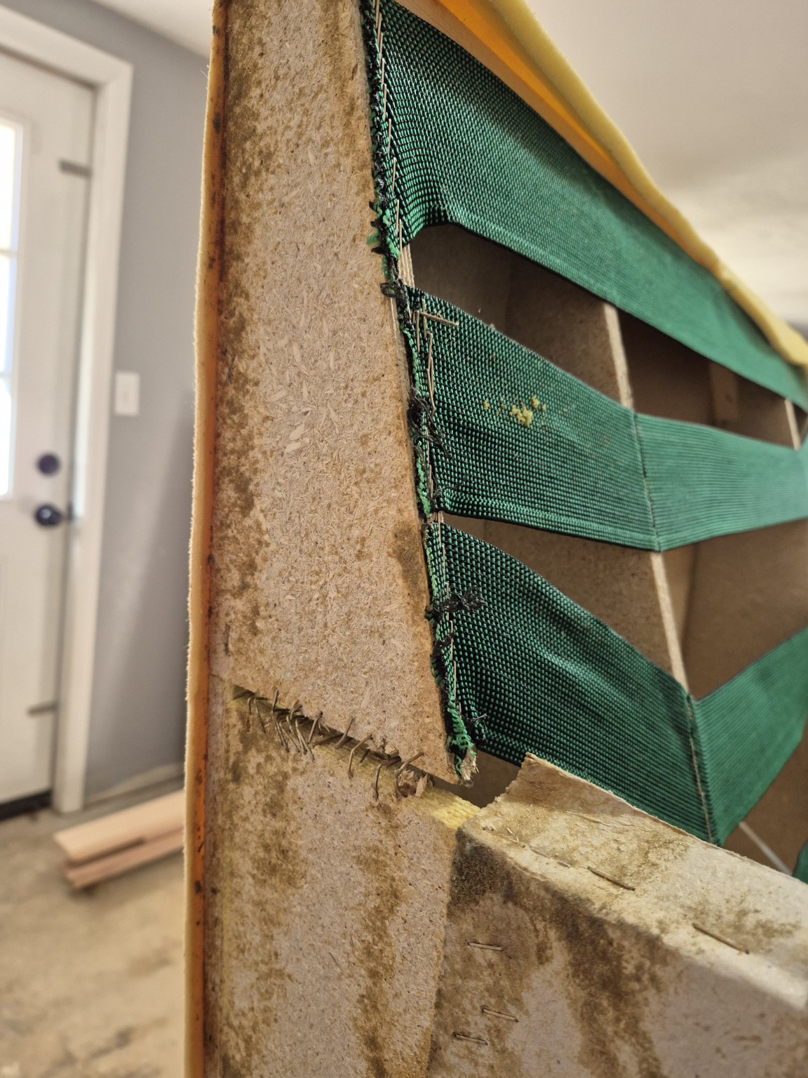 Original green webbing attached to particleboard with a separated connection below